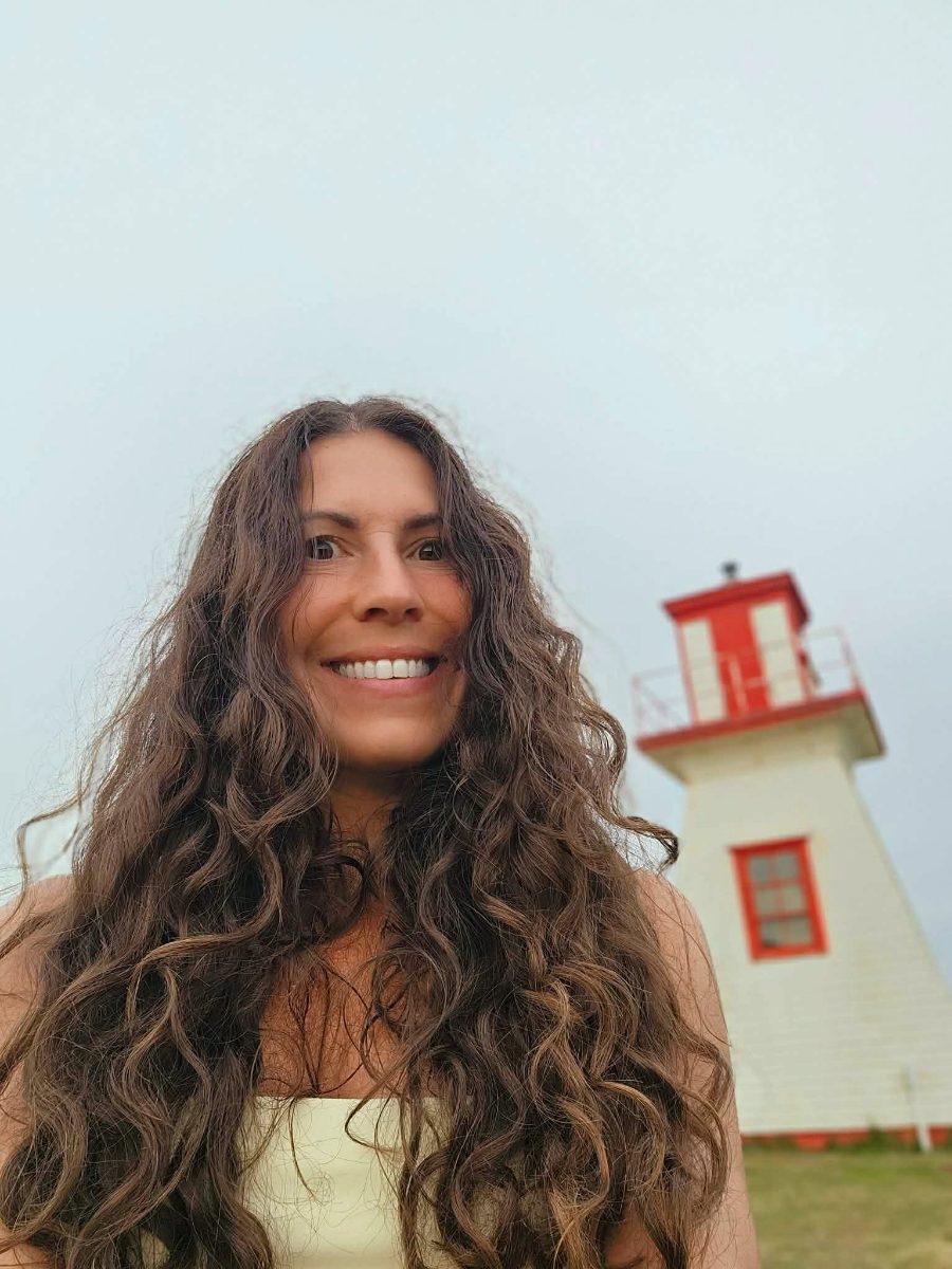 Émilie souriante devant un phare blanc et rouge